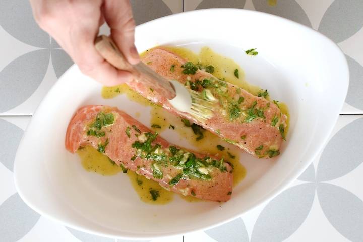 Salmon being brushed with Dijon mustard in a baking dish.