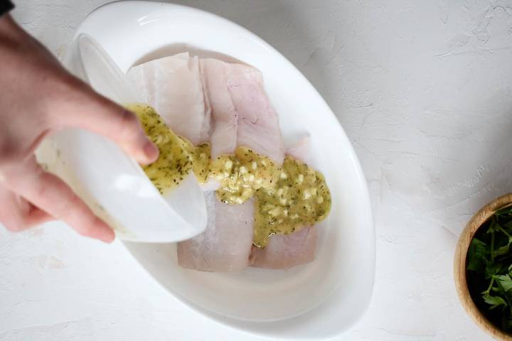 Garlic butter being poured on to cod in a baking dish.