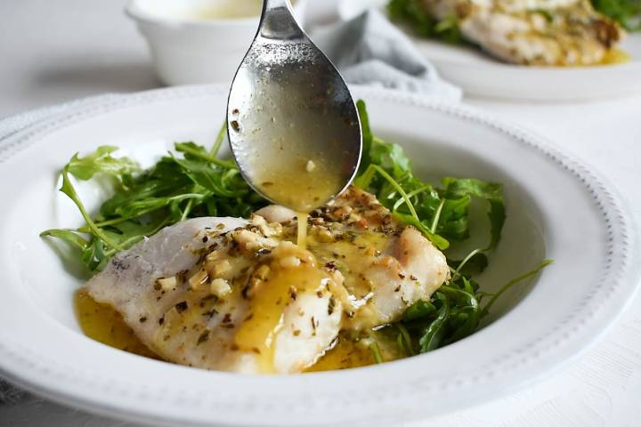 Baked cod with a lemon butter sauce being poured on top.