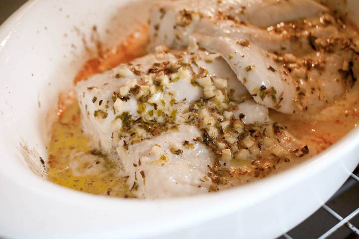 Cod baking in the oven with herbs and butter on top.