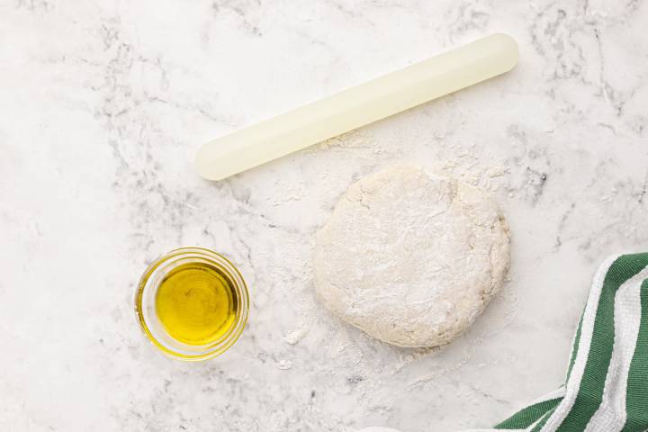 Two ingredient dough with self rising flour and yogurt on a marble board with oil and a rolling pin.