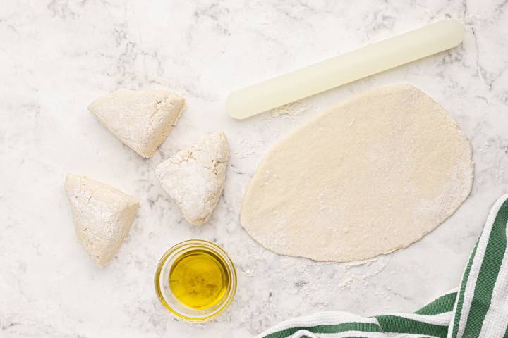 Dough being rolled into Naan pieces on a marble board.