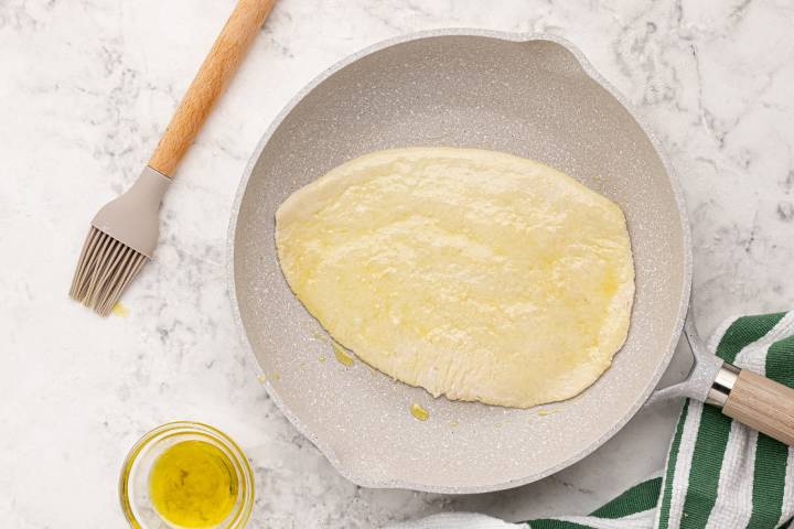 Raw Naan cooking in a skillet with olive oil.