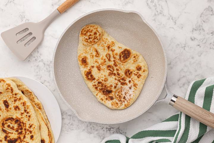 Browned Naan in a skillet with a spatula on the side.