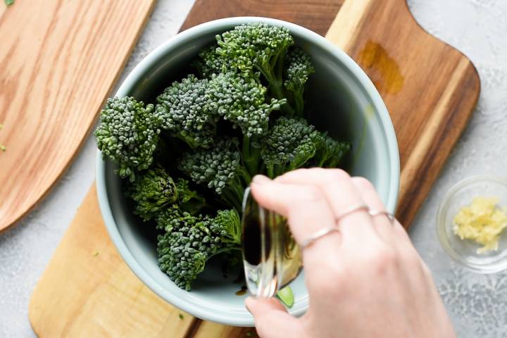 Broccolini being tossed with oil and vinegar.