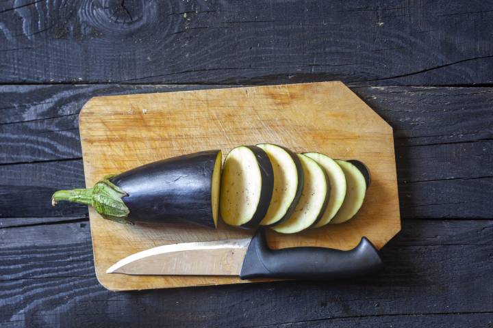 Eggplant sliced into rounds on a cutting board with a knife.