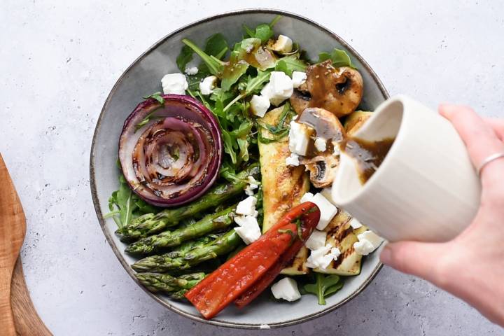 Balsamic vinaigrette being poured on top of a grilled vegetables salad.