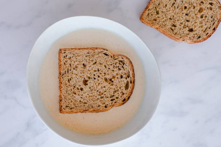 Whole wheat bread soaking in a bowl of egg custard for French toast.