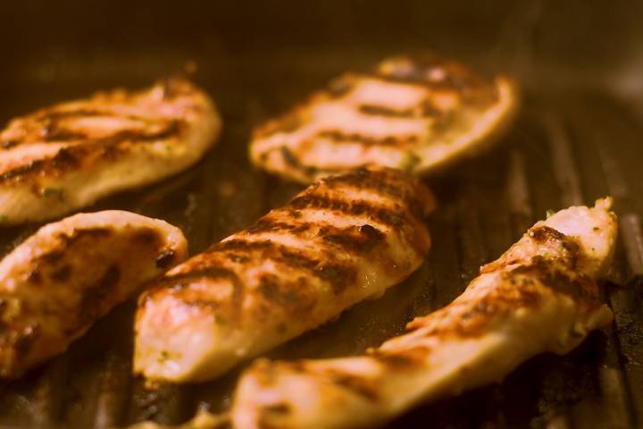 Chicken breast being grilled with grill marks.