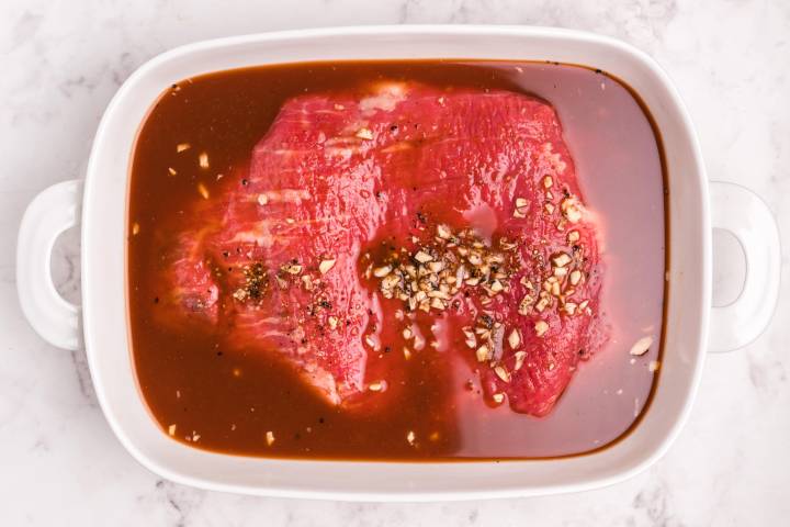 Raw flank steak marinated in a dish.