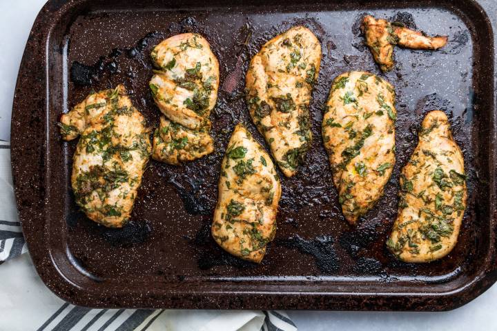 Lemon chicken breasts with parsley on a baking sheet.