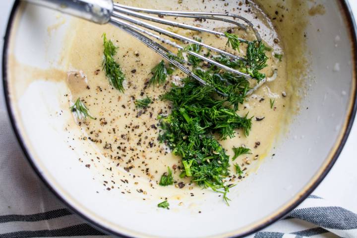 Tahini, parsley, dill, olive oil, and lemon juice in a bowl with a whisk.