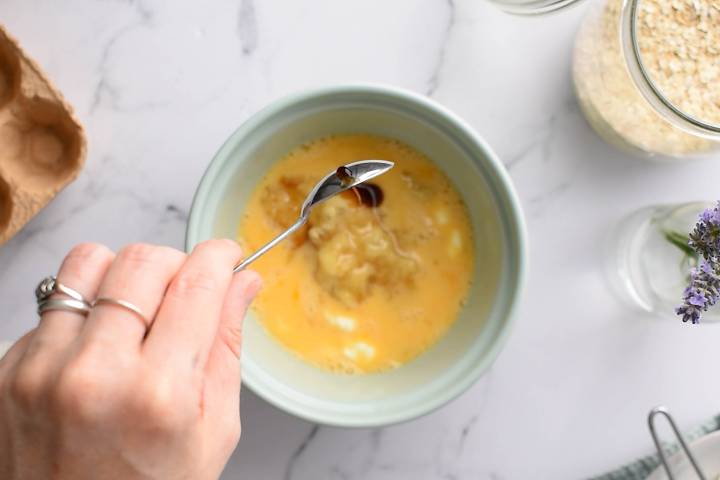 Eggs, mashed bananas, yogurt, and maple syrup being stirred in a bowl.