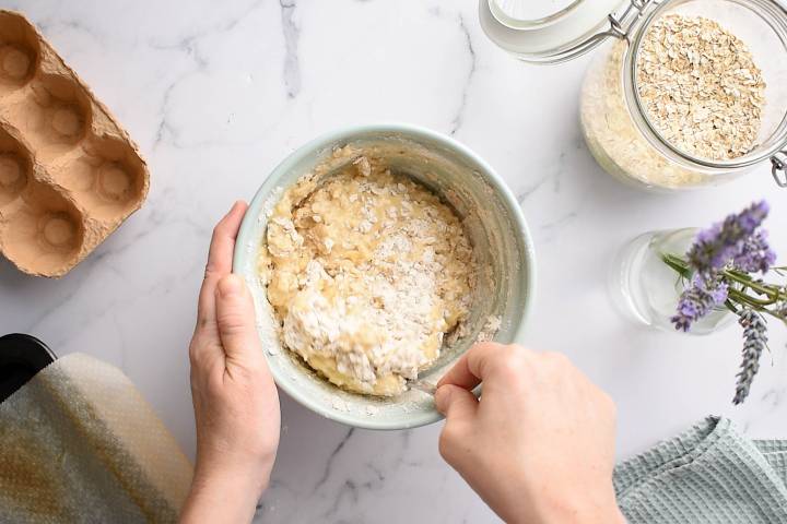 Oatmeal being stirred into an egg and banana mixture for banana bread.