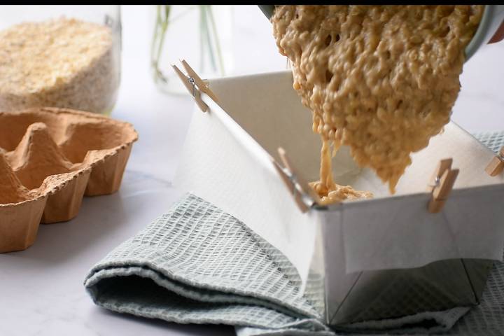 Oatmeal and banana mixture being poured into a bread pan.