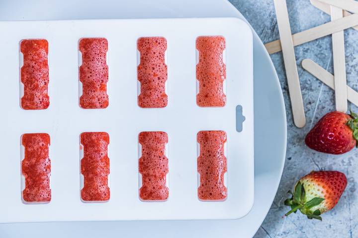 Strawberry puree being poured into a popsicle mold.