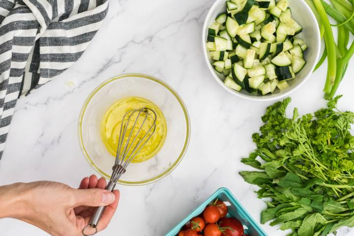 Olive oil, lemon juice, garlic, and pepper being whisked in a bowl.