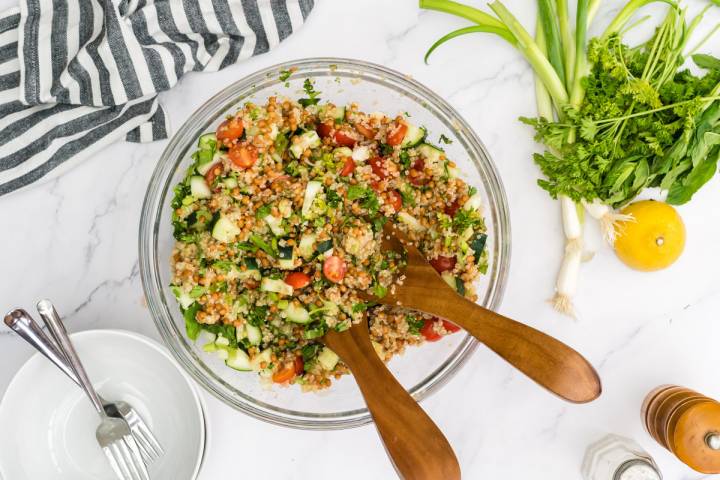 Wooden tongs tossing together quinoa tabbouleh with lentils.