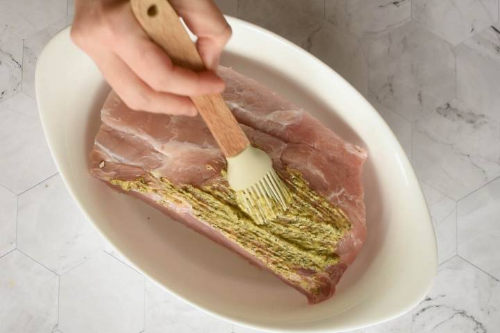 Mustard herb sauce being brushed on a pork roast.