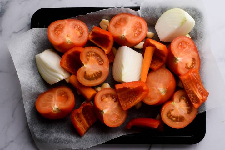 Tomatoes, carrots, onion, and garlic on a baking sheet.