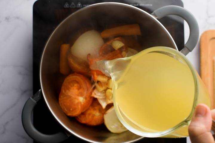 Vegetable broth being added to a pot of roasted vegetables.