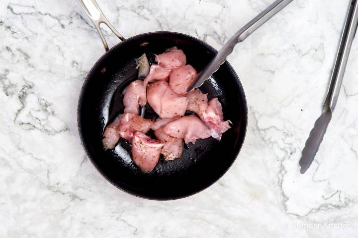 Chicken breast with Italian seasoning cooking in a skillet.