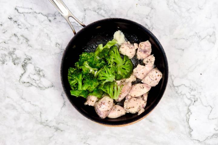 Chicken breast and broccoli cooking in a skillet for alfredo.