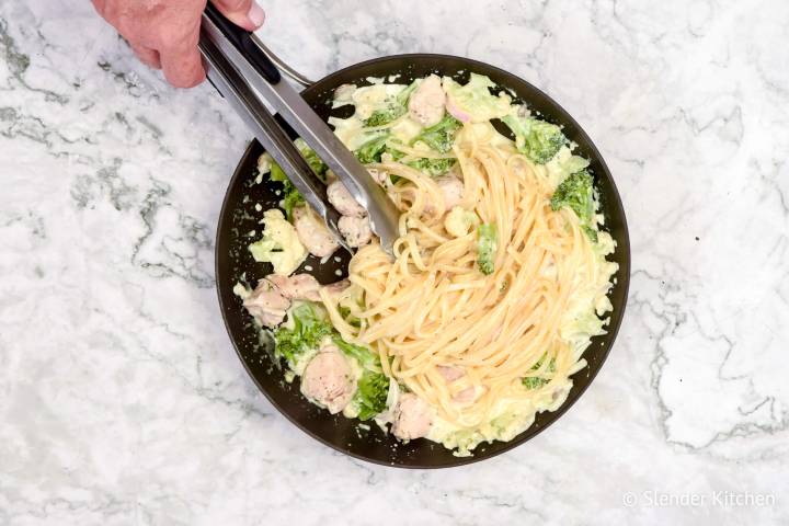 Skinny chicken alfredo pasta being stirred with tongs in a skillet.