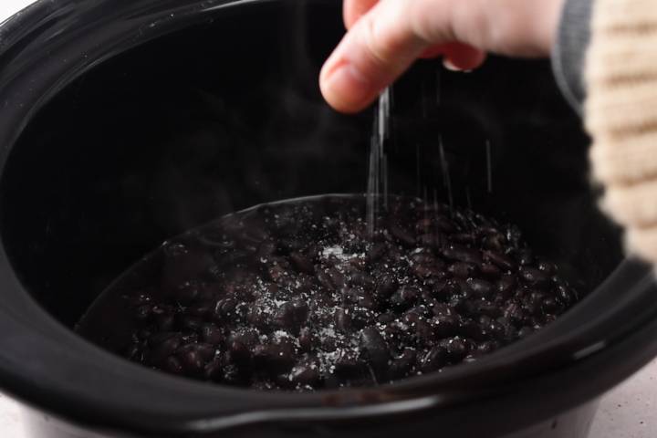 Crockpot black beans being sprinkled with salt.