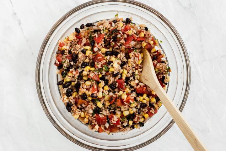 Cooked brown rice, corn, black beans, cilantro, spices, and barbecue sauce in a bowl.