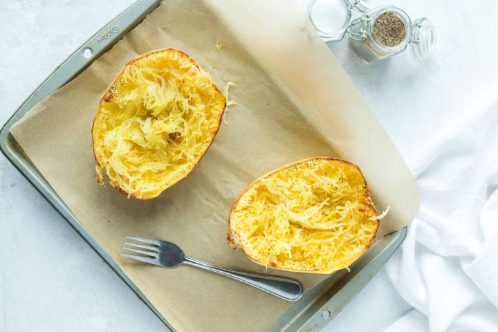 Two roasted spaghetti squash halves on a baking sheet.