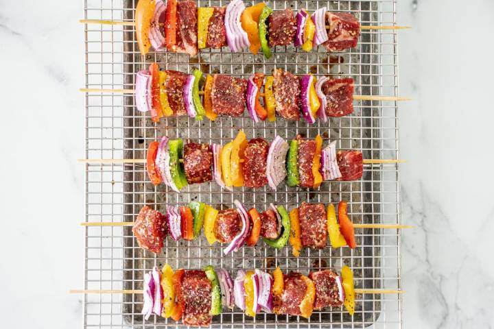 Beef kabobs with red onions and bell peppers on wooden skewers with teriyaki sauce.