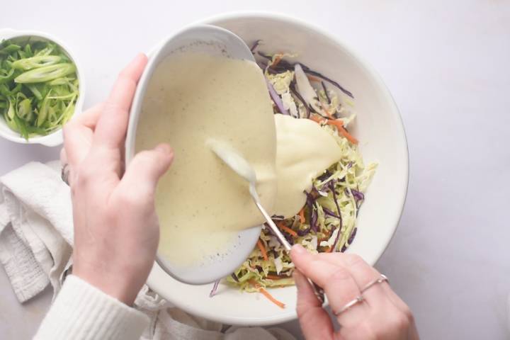 Coleslaw dressing being poured over shredded cabbage and carrots. 