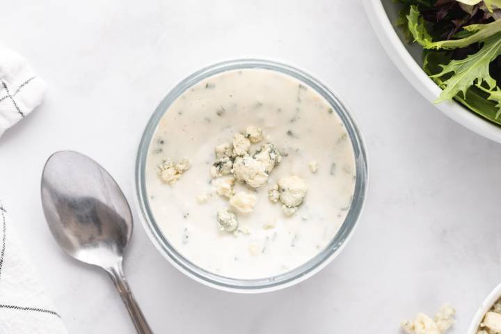 Mixed blue cheese yogurt dressing in a glass bowl with blue cheese crumbles on top.