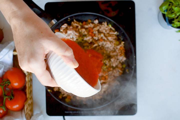 Crushed tomatoes being added to a skillet with ground turkey.