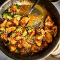 Stir fried orange chicken with broccoli in a heavy skillet with sesame seeds on top.