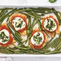 Healthy sheet pan chicken parmesan with green beans on a white sheet pan.