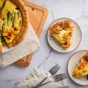 Asparagus quiche with eggs, shredded cheese, asparagus, and red onions cooked in a golden brown crust and served on plates.