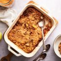 Baked apple cinnamon oatmeal in a baking dish with tender apples and a spoon.