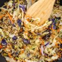 Cabbage stir fry in a black skillet with sliced green cabbage, carrots, and soy sauce.