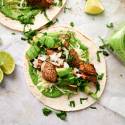 Carne asada tacos with tender steak, cilantro, onion, lime juice, avocado, and green salsa in two corn tortillas.