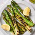 Grilled asparagus with charred edges on a plate with lemon, salt, and pepper.