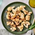 Grilled cauliflower with browned edges on a plate with red pepper flakes, salt, pepper, and olive oil.