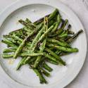 Grilled green beans served on a plate with fresh lemon, salt, and pepper.