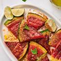 Grilled watermelon on a platter served with chili powder, lime wedges, and fresh mint.