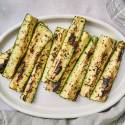 Grilled zucchini spears with dark grill marks served on a platter with olive oil, salt, pepper, and garlic.