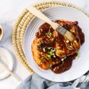 Honey chipotle grilled chicken on a plate with sliced green onions and honey chiptole sauce.