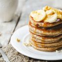 Banana oatmeal pancakes served in a stack with sliced bananas and maple syrup.