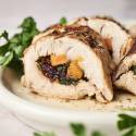 Stuffed turkey tenderloin with sweet potatoes, spinach, and dried cranberries sliced and served on a plate with parsley. 