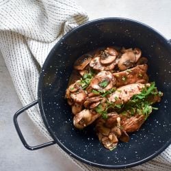 Balsamic chicken and mushrooms with fresh thyme and parsley in a bowl with a white napkin.